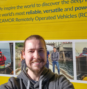 Technology student standing in front of the company's wall for a picture.