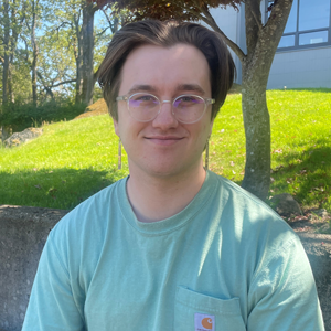 A young man with classes sitting outside a school building.