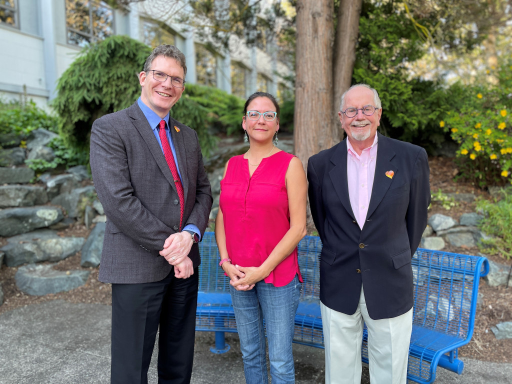 Three people pose outdoors for a photo. Left to right: a man, a woman and a man.