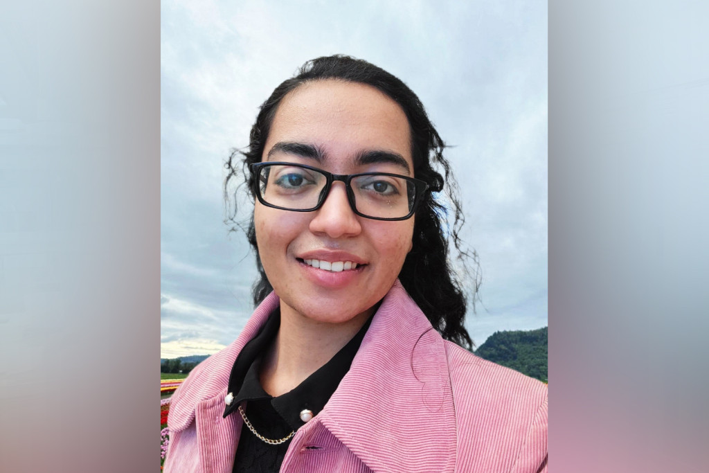 Outdoor photograph of Monika - a young woman wearing a pink jacket and dark glasses. She has long dark hair brushed back off her face.