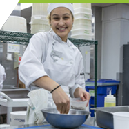 A culinary arts apprentice preparing food in a professional, industrial kitchen.