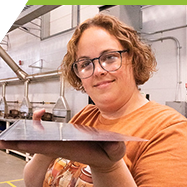 A women in an workshop holds up a piece of sheet metal.