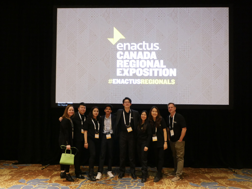 A group of students stand in front of a screen on a stage