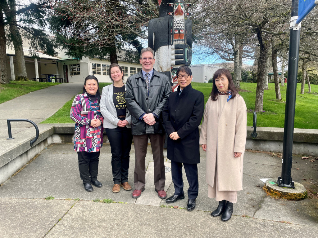 A group of five people pose for photograph next to a totem on the Interurban campus.