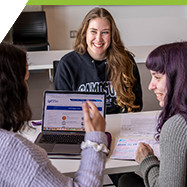 group of three students in discussion with laptop and textbooks in view