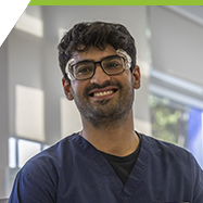 Ansh smiling towards the camera, wearing his safety glasses and rags at the Campus Dental Clinic.