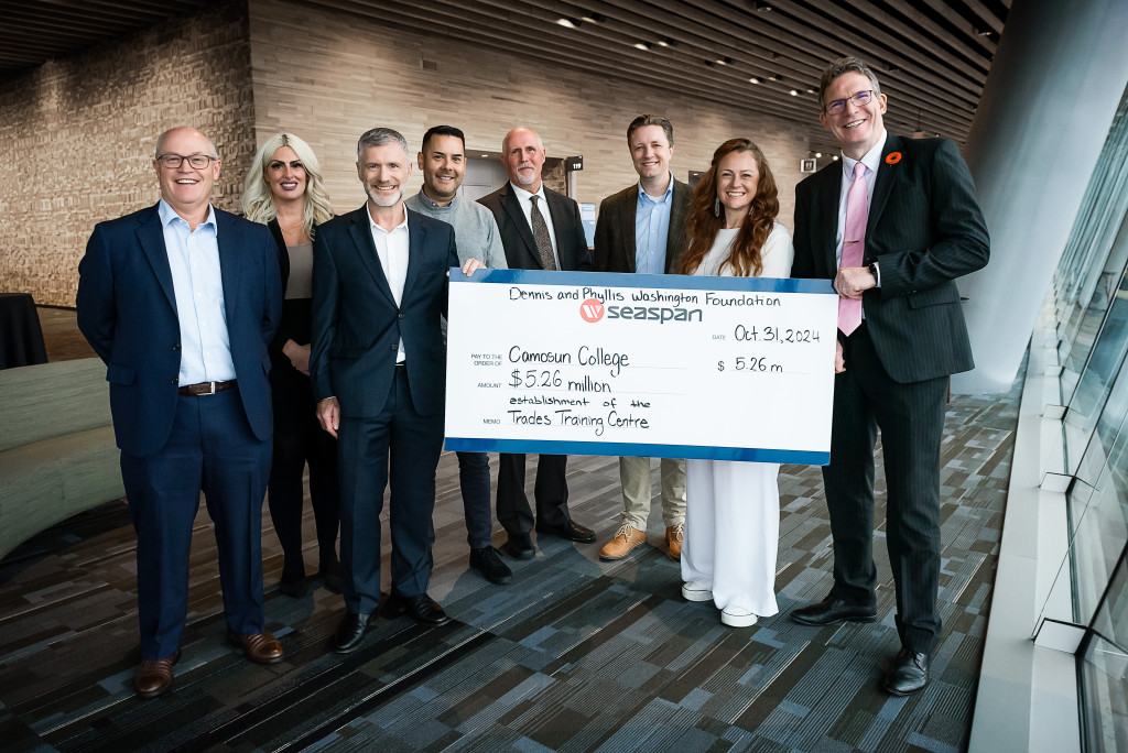 An indoor photograph of eight group of people wearing business suits. Two people are holding an over-sized cheque marked out to pay Camosun College $5.26 million to establish a trades training centre.