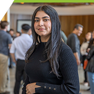 A woman in a black shirt stands in a busy room of people.