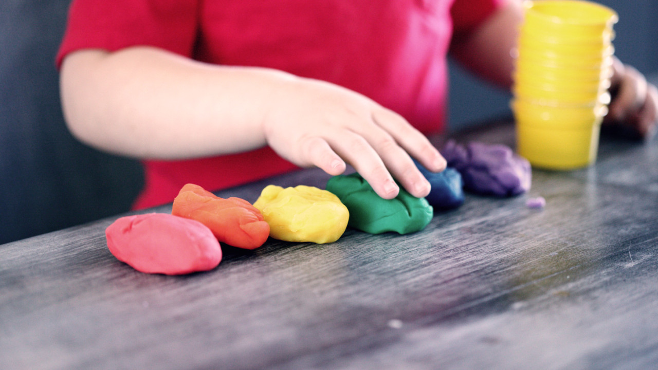 a toddler plays with a rainbow of playdough