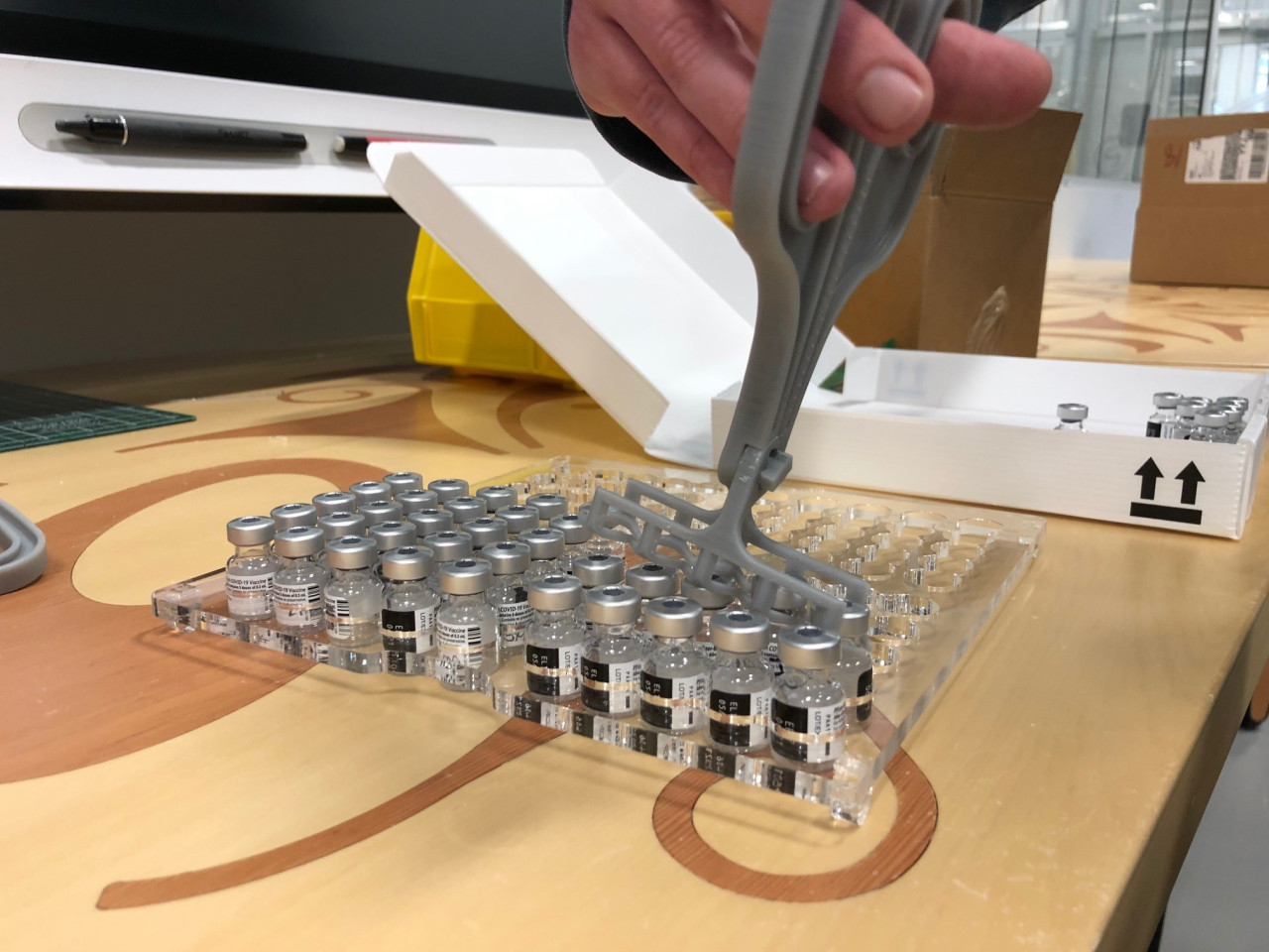 A plastic grey coloured grip lifts vials of the COVID-19 vaccine into an acrylic tray