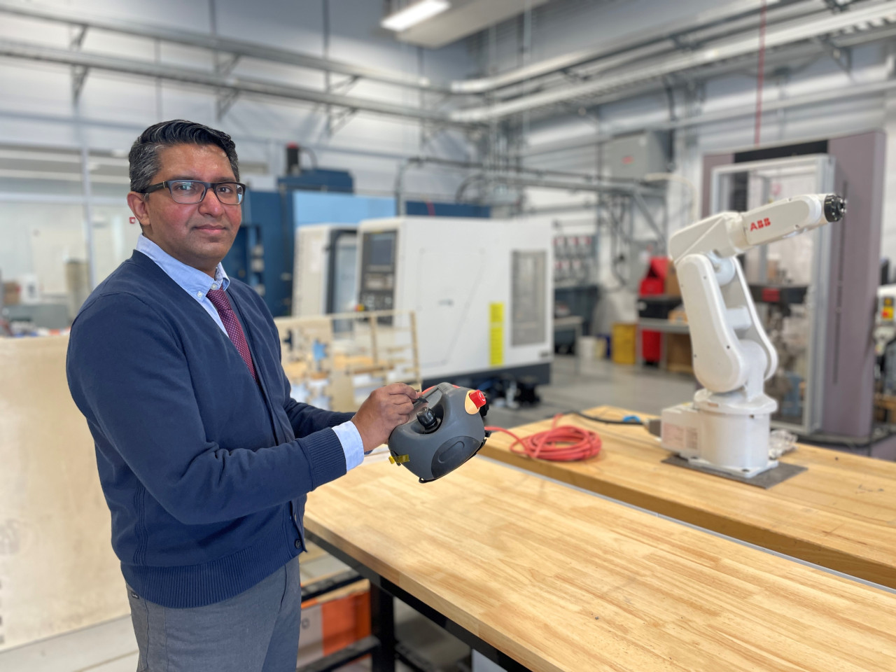 Photo of Imtehaze Heerah controlling a robotic arm while standing in a large industrial space