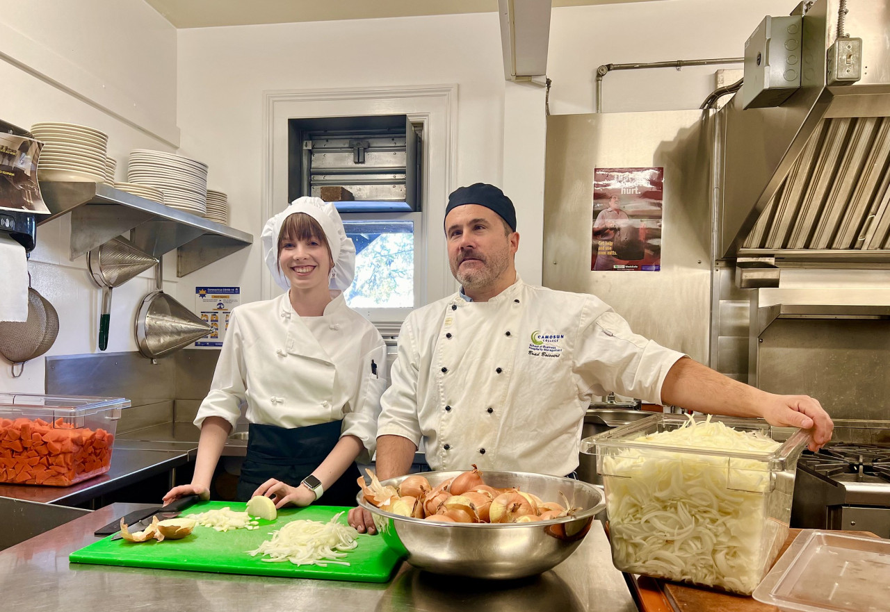 Student and instructor in the kitchen pose for a photo, taking a break form cutting onions