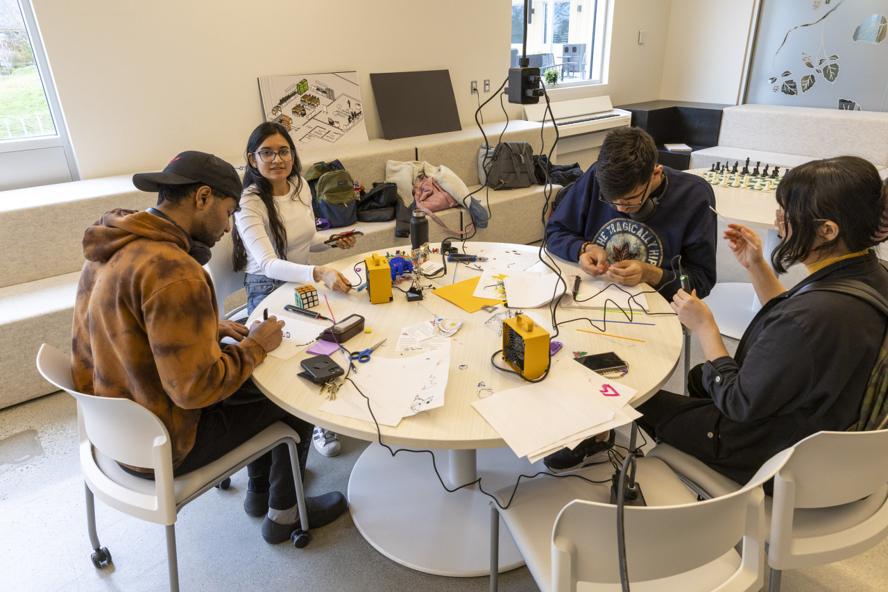 A diverse group of people sitting around a table in the Makerspace. They're working on a tech project.