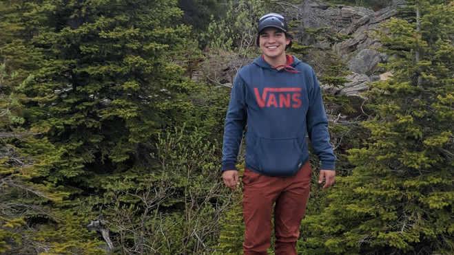 A young  Cree man poses for a photo in the mountains. 